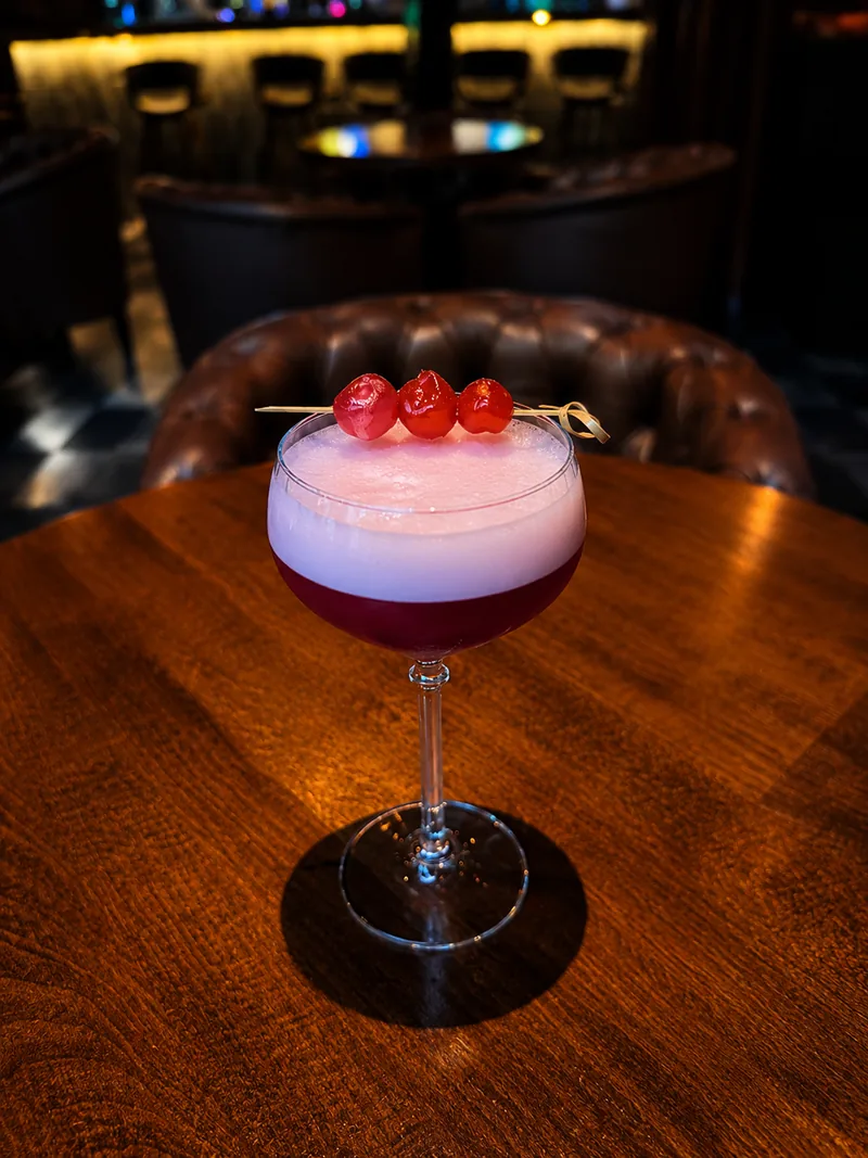 Koktajl w stylu Clover Club z wiśniami na orzechowym stoliku w Fajka Bar Lounge
